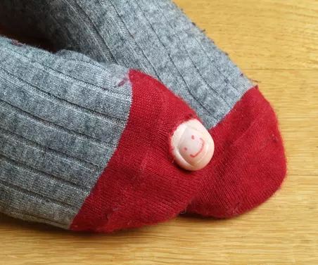 Socken mit roter Fußspitze und einem Loch. Der große Zeh guckt aus dem Loch heraus